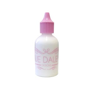 May include: A white bottle with a pink dropper top. The bottle has the text "SUE DALE DESIGNS" in pink script. The bottle is filled with a white liquid. The dropper top is a light pink color.