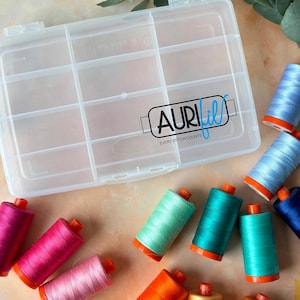 May include: A clear plastic storage box with the black and blue Aurifil logo and the text Every Stitch Counts printed on the lid. Surrounding the box are multiple sewing thread spools in various colors including pink, teal, blue, and orange.