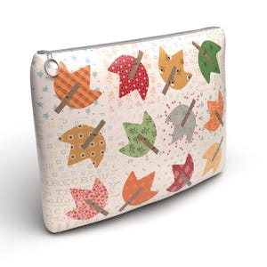 May include: A white zippered pouch with a patchwork design of colorful leaves. The leaves are made of different fabrics and have a rustic, vintage look. The pouch is perfect for storing small items like makeup, jewelry, or craft supplies.