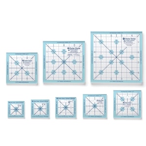 May include: A collection of clear, square quilting rulers with blue grid lines and floral accents. Sizes range from 1.5 inches to 6 inches. The text "Cute Cuts Trim-it Ruler" is visible on each ruler.