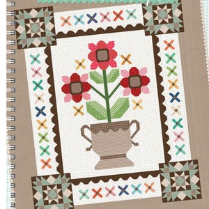 Peut inclure: Un livre de motifs de courtepointe intitulé "Prim & Proper" par Lori Holt de Bee in My Bonnet Co. La couverture présente un motif floral avec des fleurs rouges, roses et vertes dans un pot brun sur fond blanc.