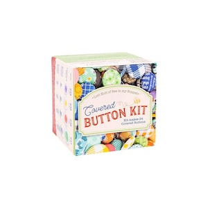 May include: A Covered Button Kit in a box, filled with colorful fabric-covered buttons. The box features the text "Covered Button Kit" and "Kit makes 24 Covered Buttons". The buttons are in various patterns and colors.