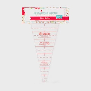 Puede incluir: Regla de pastel de plástico transparente con marcas rojas y el texto "Pie Ruler". La regla es triangular y tiene medidas en centímetros. El embalaje muestra "Sew Simple Shapes" y "Pie Ruler".