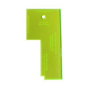 May include: A neon green quilt binding ruler with text that reads "2.25 Binding width" and "2.5 Binding width". The ruler has a hole and text that says "Made in USA" and "Patent Pending". The text "QUILT BINDING RULER" is also visible.