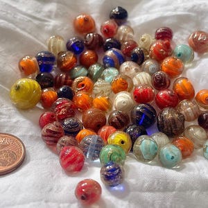 May include: A collection of colourful glass beads in various shapes and sizes. The beads are a mix of red, orange, yellow, green, blue, and white. Some of the beads have a speckled or marbled effect.