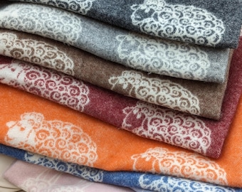 May include: A stack of colorful blankets with a sheep design. The blankets are made of a soft, fuzzy material and are perfect for cuddling up on the couch.