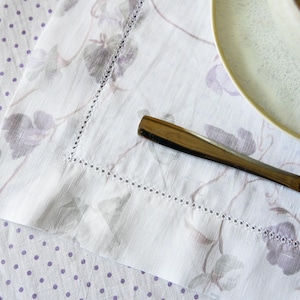 May include: A white linen tablecloth with a delicate floral pattern and a silver knife on top. The tablecloth has a subtle polka dot pattern.
