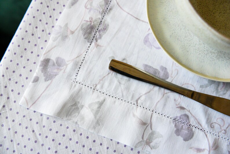 May include: A white linen tablecloth with a delicate floral pattern and a silver knife on top. The tablecloth has a subtle polka dot pattern.