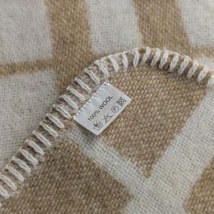 May include: A close-up of a beige and white checkered throw blanket with a white label that reads "100% Wool" and has care instructions.