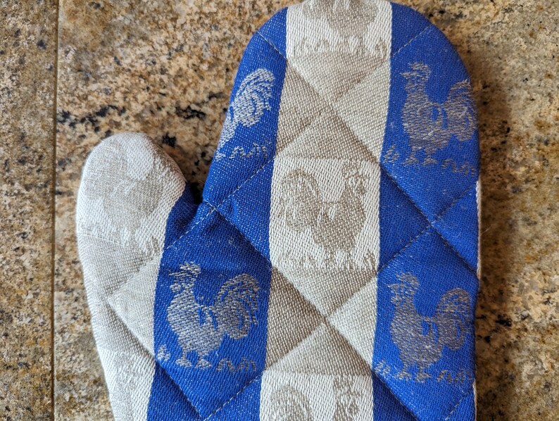 Puede incluir: Manopla de horno acolchada azul y blanca con un dise&ntilde;o de gallo. La manopla est&aacute; hecha de una tela suave y texturizada.