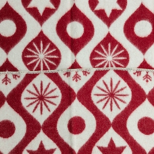 Puede incluir: Primer plano de una tela estampada blanca y roja. El dise&ntilde;o presenta un patr&oacute;n repetitivo de formas de gotas rojas, c&iacute;rculos, estrellas y dise&ntilde;os en forma de copo de nieve. La tela est&aacute; dividida por una costura blanca en zigzag.