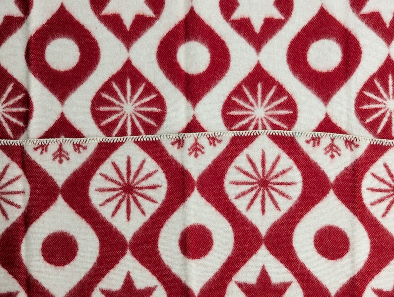 Puede incluir: Primer plano de una tela estampada blanca y roja. El dise&ntilde;o presenta un patr&oacute;n repetitivo de formas de gotas rojas, c&iacute;rculos, estrellas y dise&ntilde;os en forma de copo de nieve. La tela est&aacute; dividida por una costura blanca en zigzag.