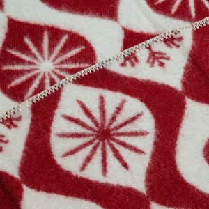 Puede incluir: Primer plano de un textil estampado en rojo y blanco. El dise&ntilde;o presenta un patr&oacute;n repetitivo de explosiones de estrellas estilizadas y formas curvas. Los bordes est&aacute;n acabados con una puntada en zigzag blanca.