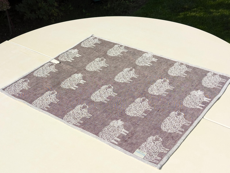 May include: A brown throw blanket with a white sheep pattern. The blanket is made of a soft, textured fabric.