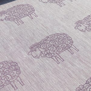 May include: A white fabric with a repeating pattern of purple sheep. The sheep are stylised and have a curly wool design.