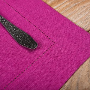May include: A close-up of a pink linen placemat with a silver, ornate spoon on top.