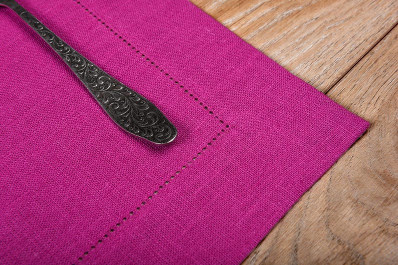 May include: A close-up of a pink linen placemat with a silver, ornate spoon on top.