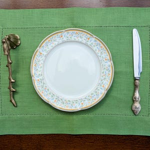 Könnte beinhalten: Ein grünes Platzset mit einem weißen Teller mit Blumenmuster, einem silbernen Messer und einem dekorativen Bronzeast.