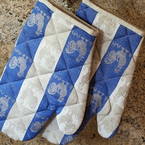 Puede incluir: Un par de guantes de horno a rayas azules y blancas con un dise&ntilde;o acolchado y un patr&oacute;n de gallo.