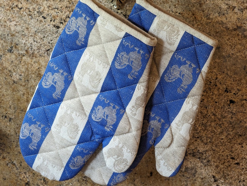 Puede incluir: Un par de guantes de horno a rayas azules y blancas con un dise&ntilde;o acolchado y un patr&oacute;n de gallo.