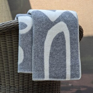 May include: A gray and white patterned throw blanket draped over a wicker chair. The blanket has a modern abstract design with white lines on a gray background.