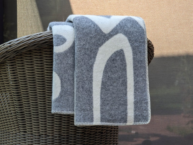 May include: A gray and white patterned throw blanket draped over a wicker chair. The blanket has a modern abstract design with white lines on a gray background.