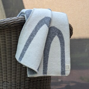May include: A white and gray wool throw blanket with a geometric pattern of arches. The blanket is folded and draped over the back of a wicker chair.