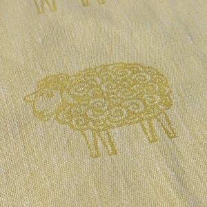 May include: A white fabric with a repeating pattern of gold sheep. The sheep are stylised and have a detailed design.