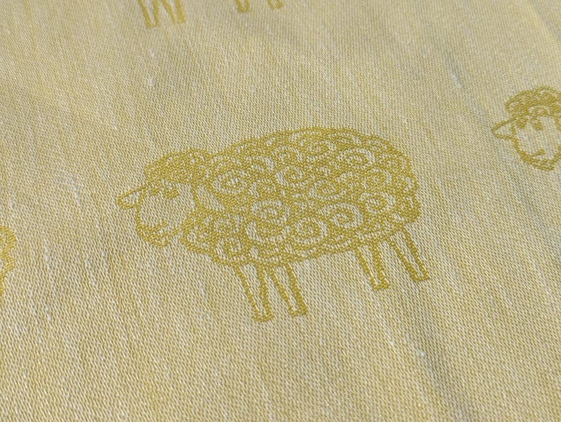 May include: A white fabric with a repeating pattern of gold sheep. The sheep are stylised and have a detailed design.