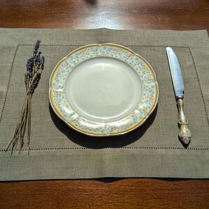 Puede incluir: Un mantel individual de lino verde con un plato de patr&oacute;n floral blanco y amarillo y un cuchillo de plata.