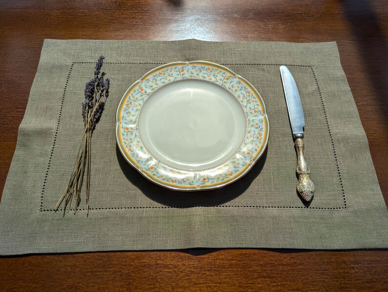 Puede incluir: Un mantel individual de lino verde con un plato de patr&oacute;n floral blanco y amarillo y un cuchillo de plata.