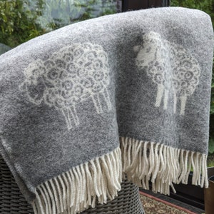 May include: A gray wool throw blanket with a white sheep design. The blanket has a fringe border.