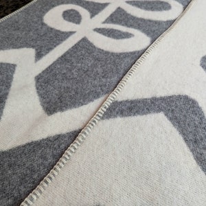May include: A gray and white woven blanket with a geometric pattern. The blanket has a white zig-zag pattern on one side and a gray loop pattern on the other side.