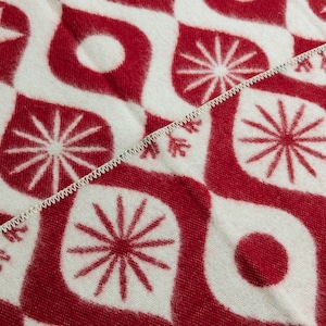 Puede incluir: Primer plano de una tela estampada en rojo y blanco. El dise&ntilde;o presenta formas de l&aacute;grima estilizadas, estrellas, c&iacute;rculos y elementos similares a copos de nieve. Una costura blanca en zigzag divide la tela diagonalmente.