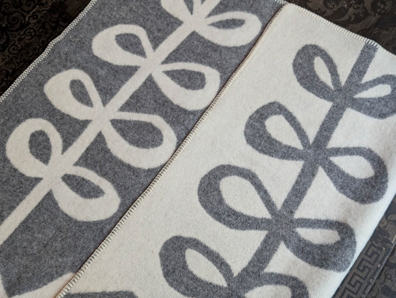May include: A gray and white throw blanket with a repeating pattern of stylized leaves. The leaves are outlined in white on a gray background and gray on a white background.