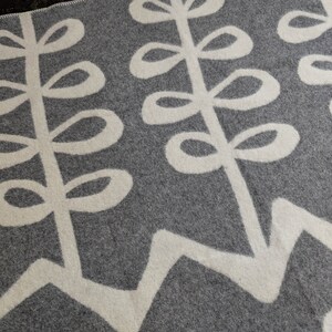 May include: A gray and white throw blanket with a repeating pattern of stylized leaves. The leaves are white on a gray background.
