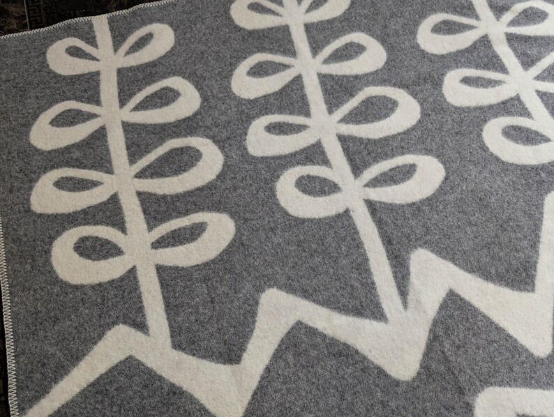 May include: A gray and white throw blanket with a repeating pattern of stylized leaves. The leaves are white on a gray background.