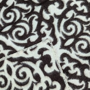 Puede incluir: Primer plano de una tela blanca con un patr&oacute;n de espiral blanco y negro. La tela tiene una costura blanca alrededor del borde.