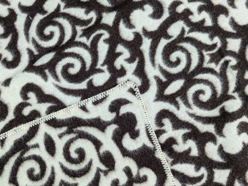 Puede incluir: Primer plano de una tela blanca con un patr&oacute;n de espiral blanco y negro. La tela tiene una costura blanca alrededor del borde.