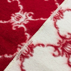 May include: Close-up of a red and white patterned blanket with a white seam running diagonally across the fabric.
