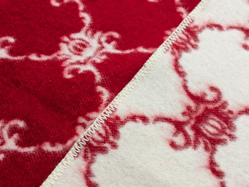May include: Close-up of a red and white patterned blanket with a white seam running diagonally across the fabric.