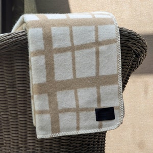 May include: A beige and white checkered throw blanket with a black label hanging over a wicker chair.