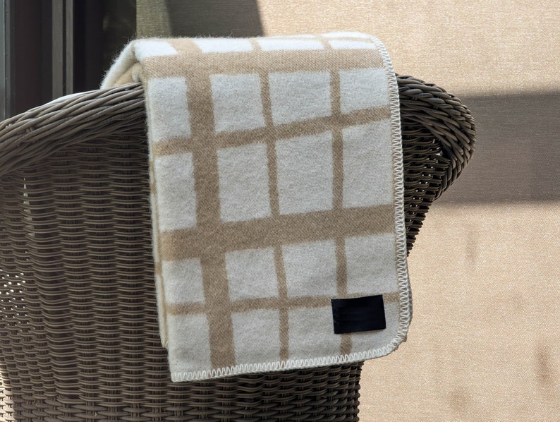 May include: A beige and white checkered throw blanket with a black label hanging over a wicker chair.