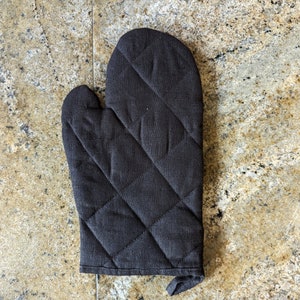 K&ouml;nnte beinhalten: Ein schwarzer, gesteppter Ofenhandschuh mit Rautenmuster.