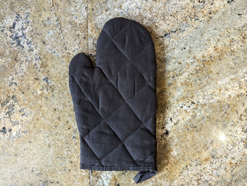 K&ouml;nnte beinhalten: Ein schwarzer, gesteppter Ofenhandschuh mit Rautenmuster.