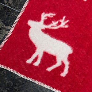 May include: Red throw blanket with a white reindeer pattern. The blanket has a white stitched border.