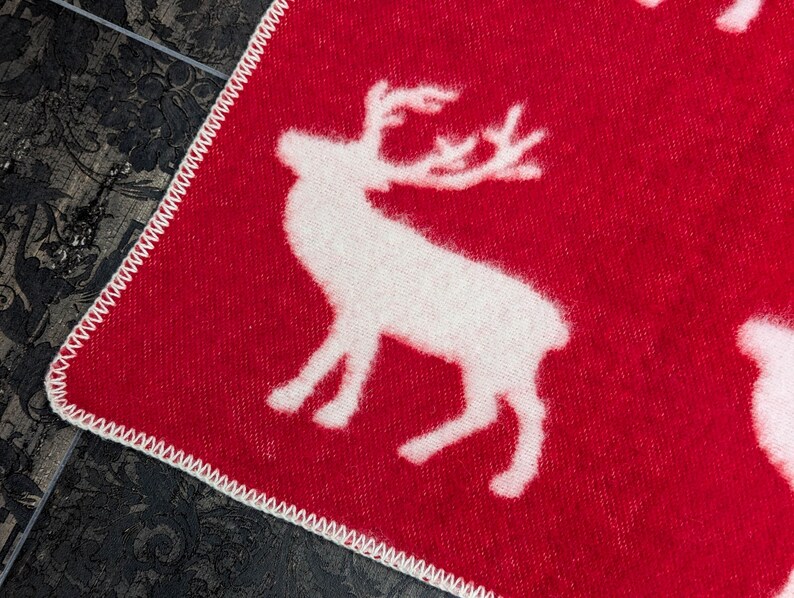 May include: Red throw blanket with a white reindeer pattern. The blanket has a white stitched border.