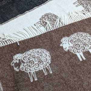 May include: A brown and white wool throw blanket with a repeating pattern of white sheep. The blanket has a fringe border.