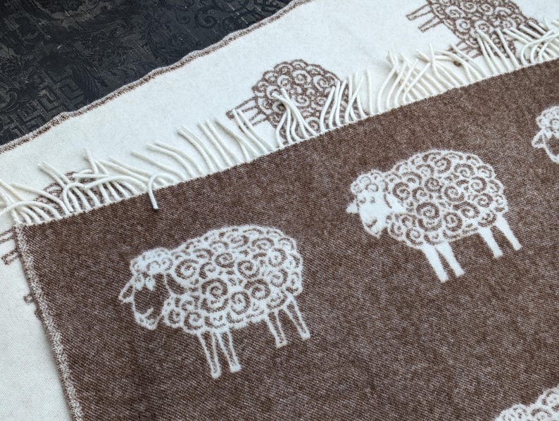 May include: A brown and white wool throw blanket with a repeating pattern of white sheep. The blanket has a fringe border.