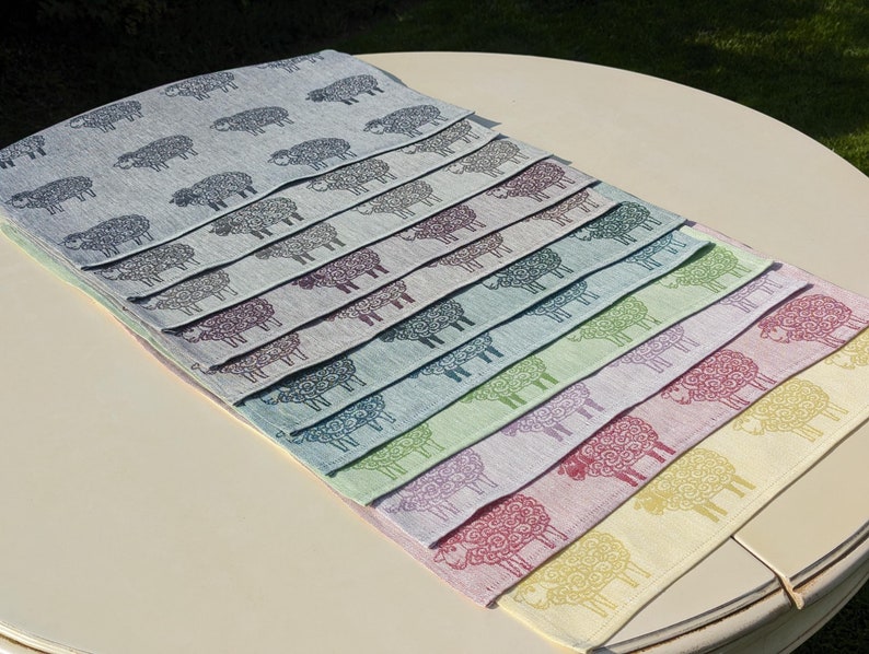 May include: A set of ten linen placemats featuring a repeating pattern of stylised sheep in various colours, including blue, green, purple, pink and yellow.